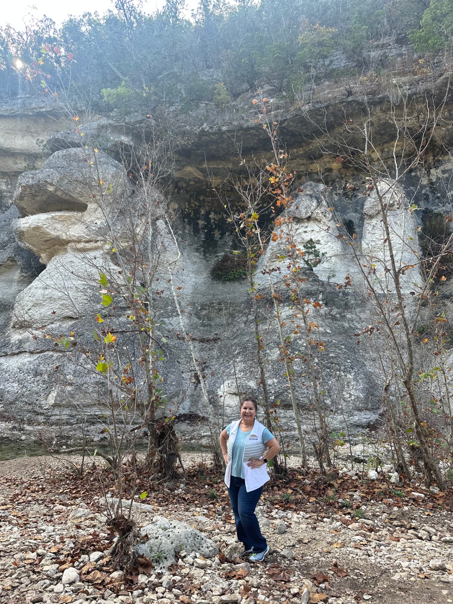 Cynthia standing on a rocky trail surrounded by trees and limestone cliffs, enjoying time outdoors.